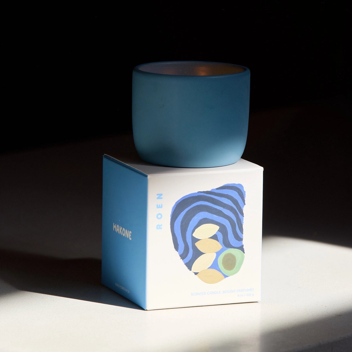 Blue candle on a white box with a blue label against a dark background
