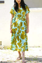 Load image into Gallery viewer, Woman wearing a floral dress standing outdoors against a white wall.