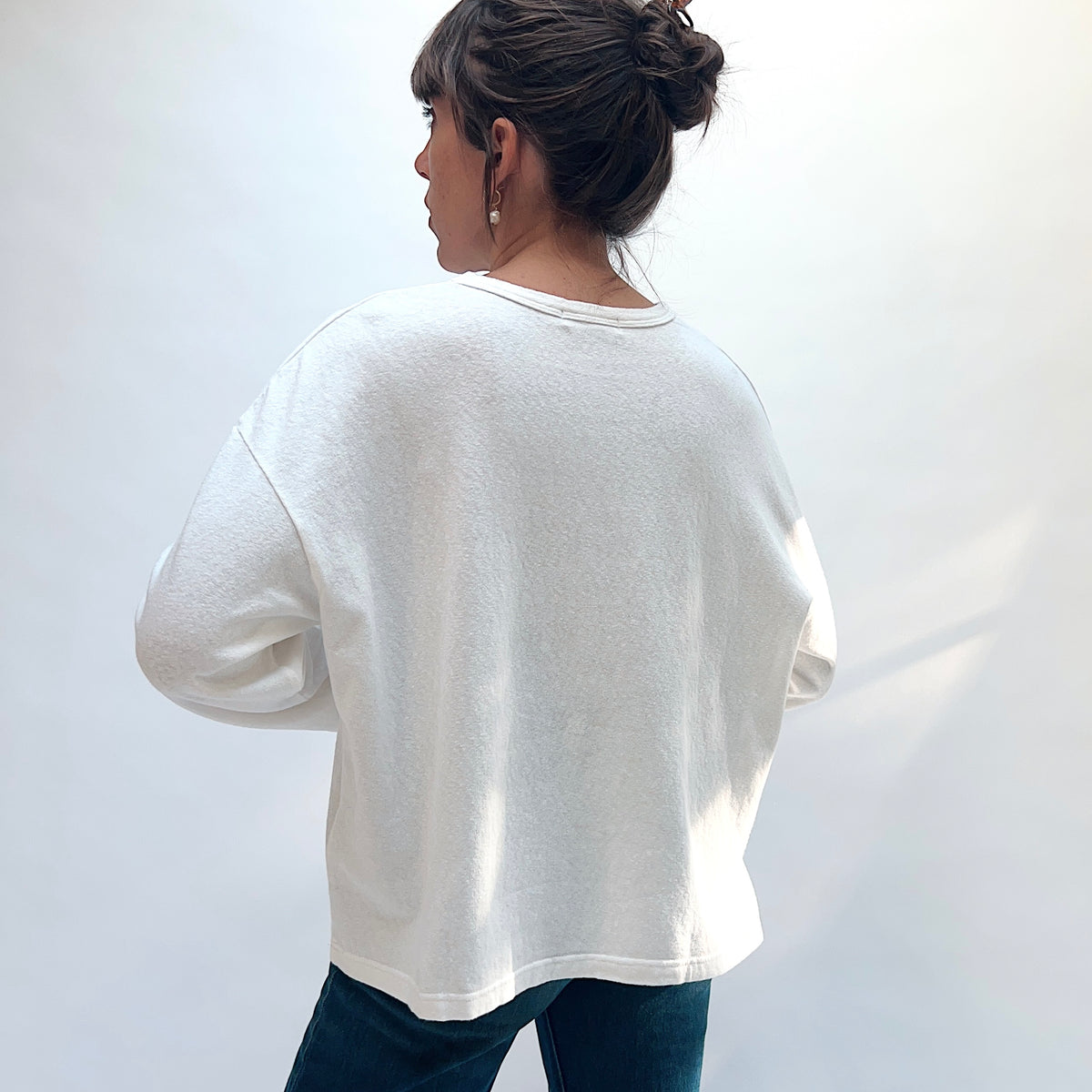 Back view of a model wearing the white cotton knit pullover, showing the plain back, dropped shoulders, and straight hem.