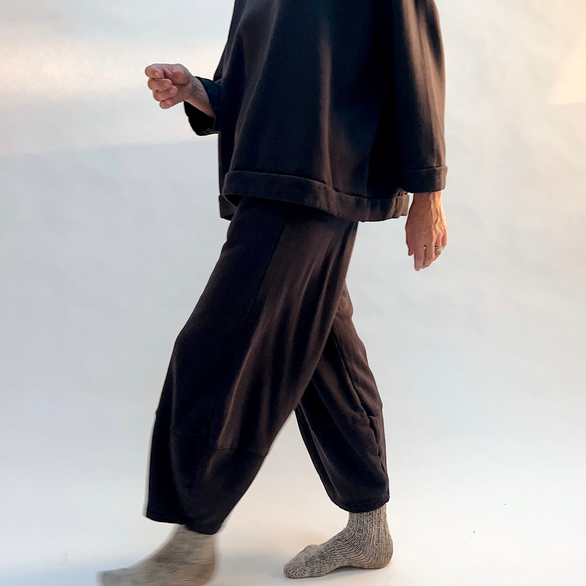 Side view of a model walking in Oliver Fleece Pant in Fig, showing the drape and curved leg shape.