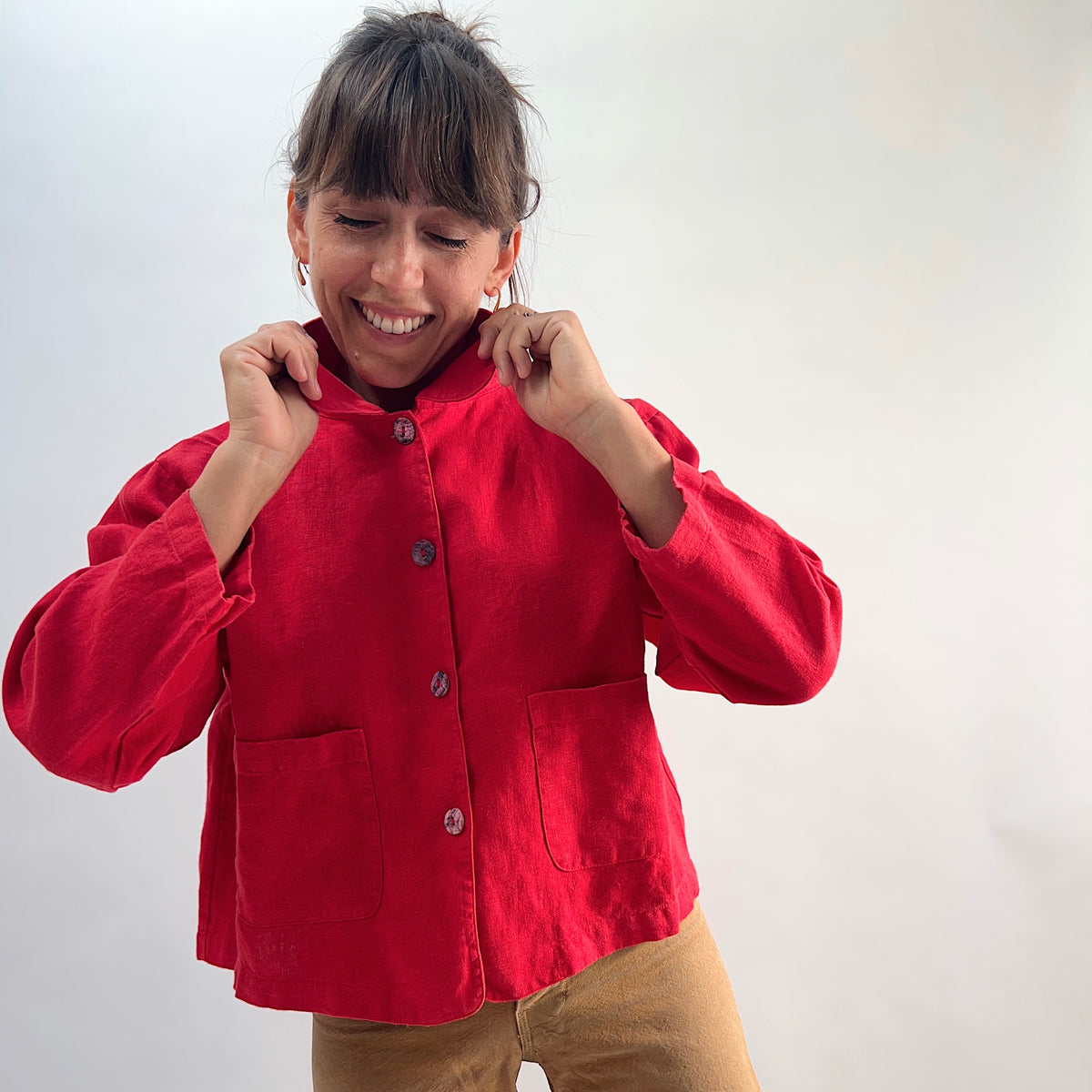 Model laughing and pulling up collar of the Bryn Walker Heavy Linen Audrey Jacket in Hawthorn, front view showing patch pockets and shell buttons