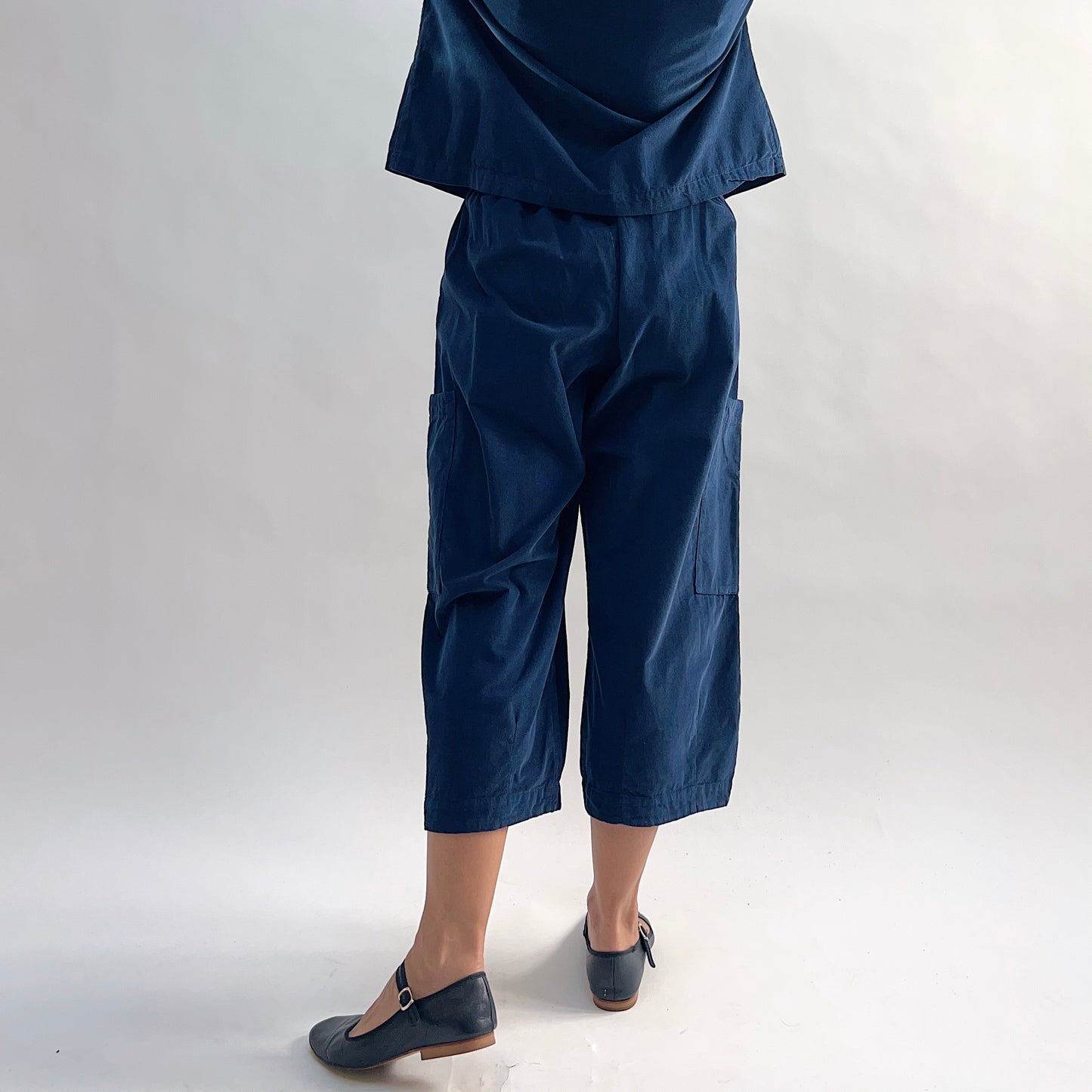 Back view of the Bryn Walker Corduroy Pasha Pants in Nova, showing elastic waistband, side leg pockets, cropped hemline, and relaxed silhouette in navy pinwheel corduroy, with black Mary Jane flats