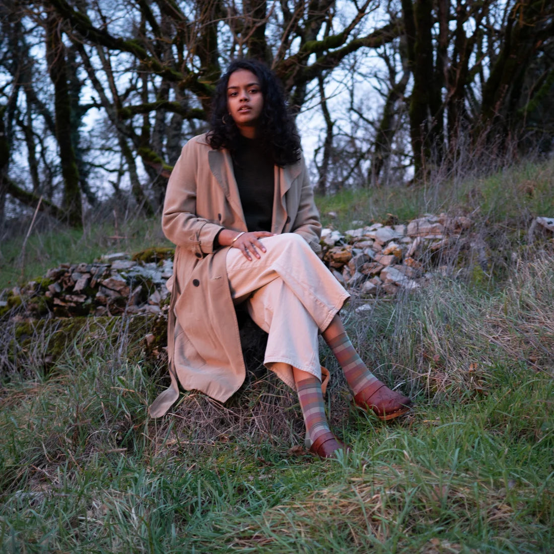Bonne Maison Sunday Plaid Socks styled on model seated outdoors, showing the crew length and muted plaid pattern in sage and dusty rose