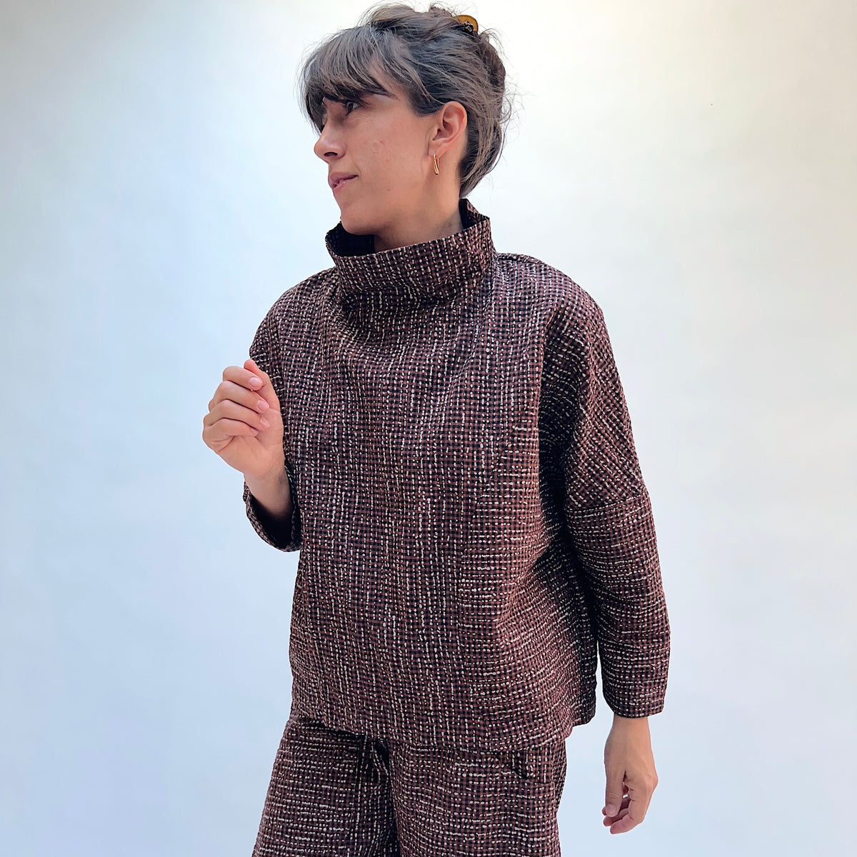 Niche Sofi Top in Cocoa Check, three-quarter front view showing the cropped hip length and high funnel neck in dark brown textured check with contrast black cuffs