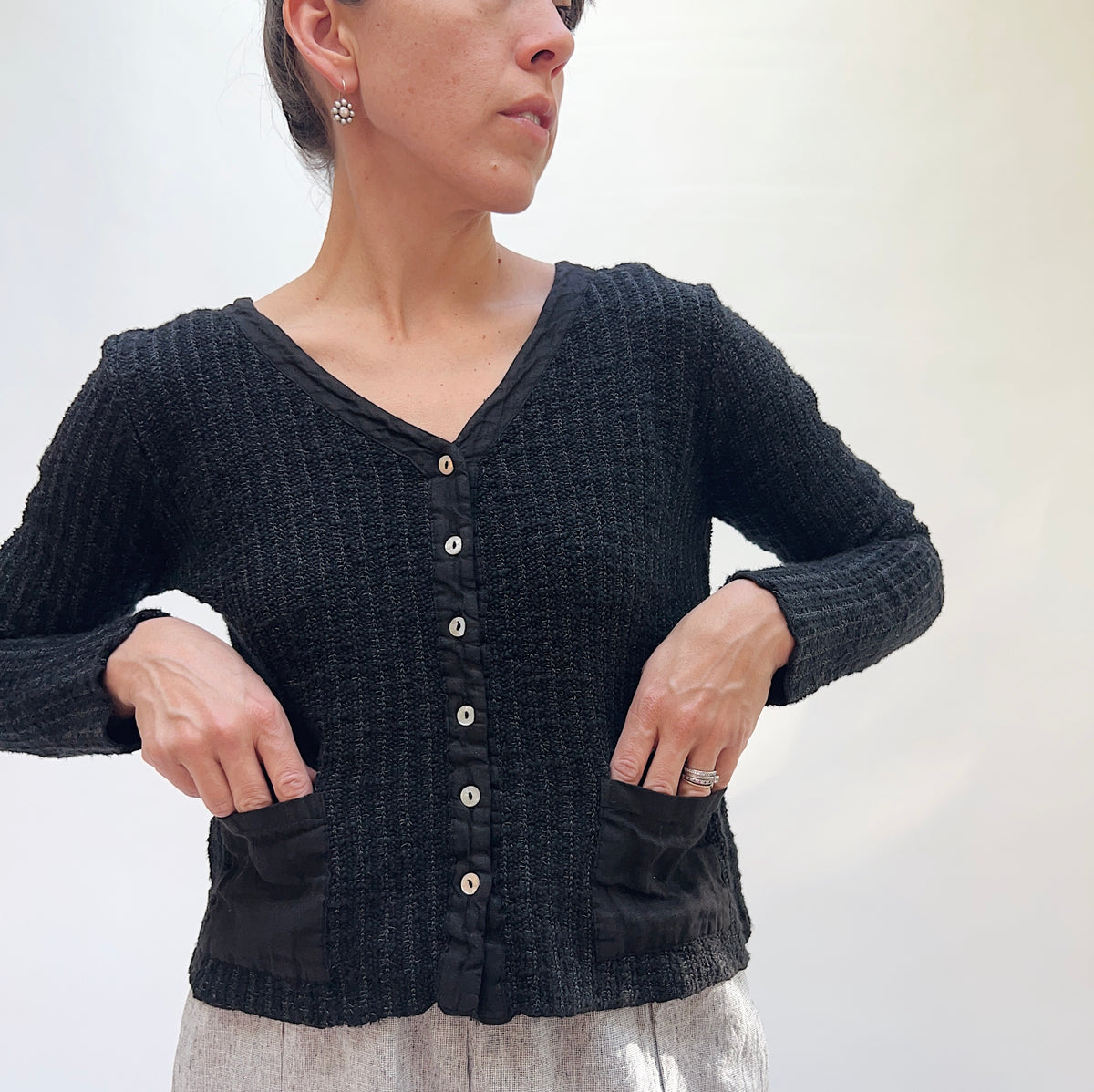 Person wearing a back textured cardigan with pockets against a white background