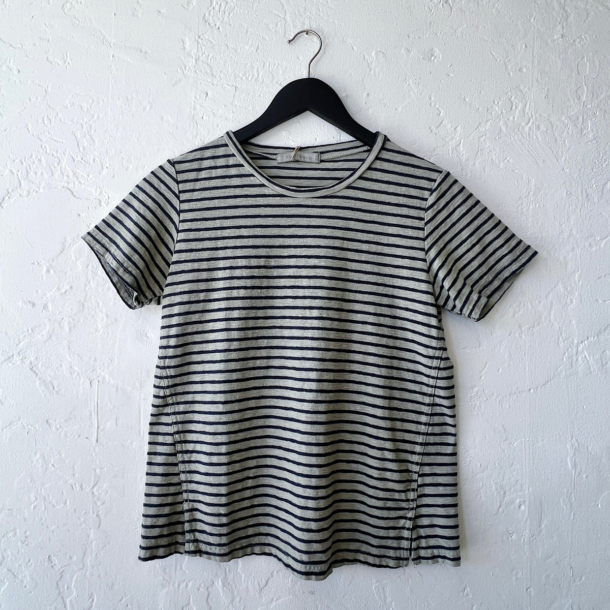 Green and black striped t-shirt on a hanger against a white wall