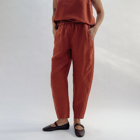 Front view of the Seamed Taper Pant in Terracotta by Yuvita, showing the elastic waistband, side pockets, and tapered ankle, styled with a matching terracotta linen tank and dark Mary Jane flats
