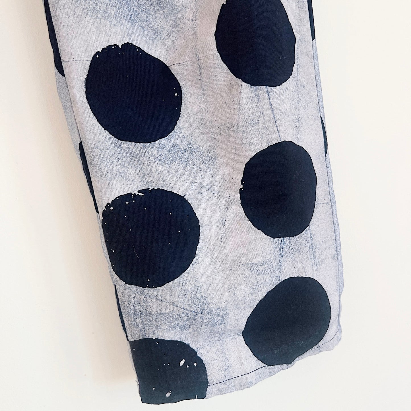 Close-up of the lower leg and hem of the Lazy Pants in Indigo Dots, showing large hand-printed black circles on a grey-white 100% cotton Batiki fabric with visible hand-dye texture and hemline detail