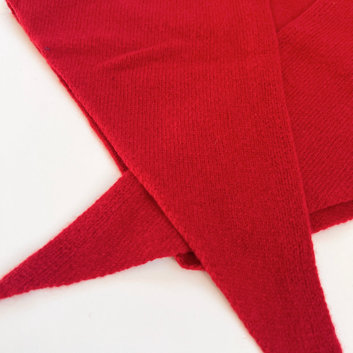 Close-up of the red merino wool scarf showing its fine knit texture, edges and overlapping pointed ends.