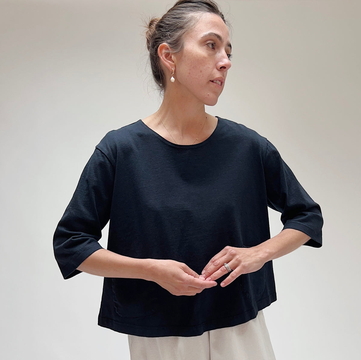 A person wearing a black, 3/4 sleeve top with two front pockets, made of cotton, in a casual setting