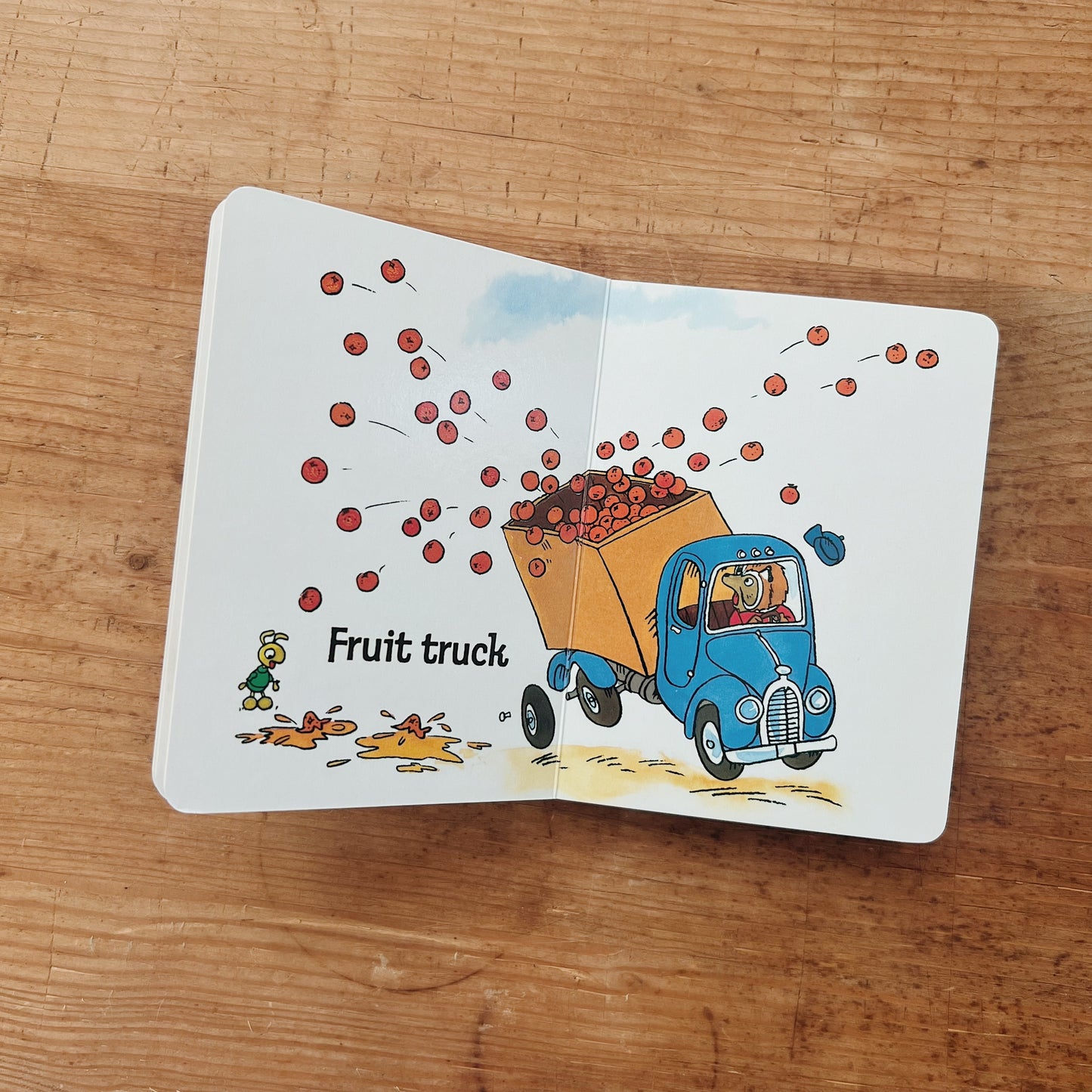Interior spread of Richard Scarry's Trucks board book showing a blue fruit truck spilling apples, with the label "Fruit truck"