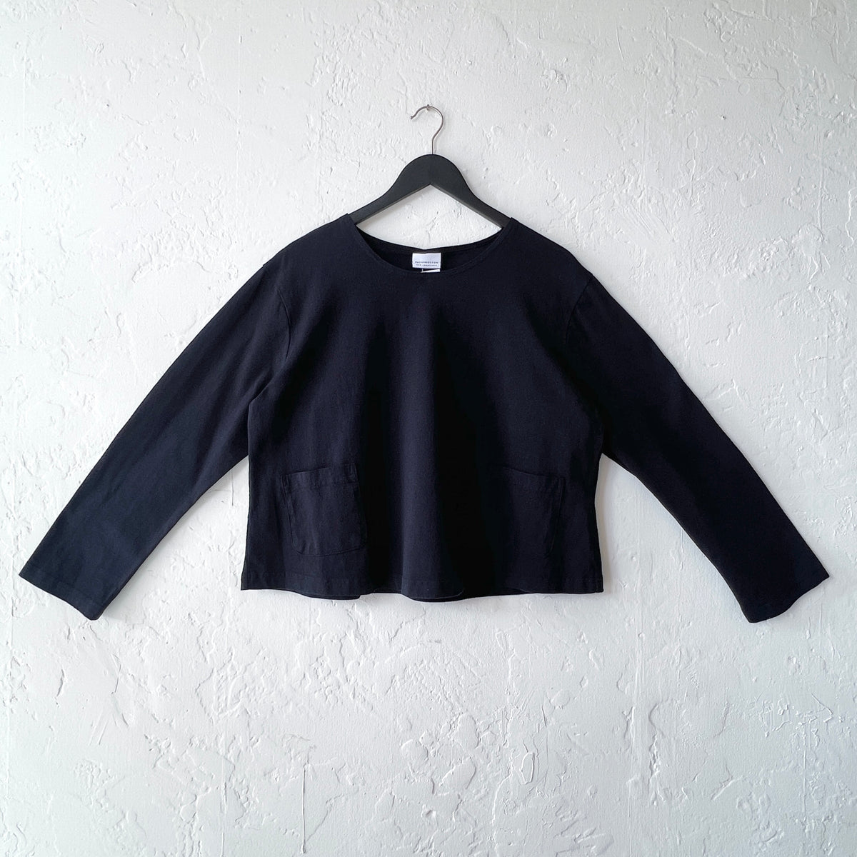 Black long-sleeve top on a hanger against a white wall