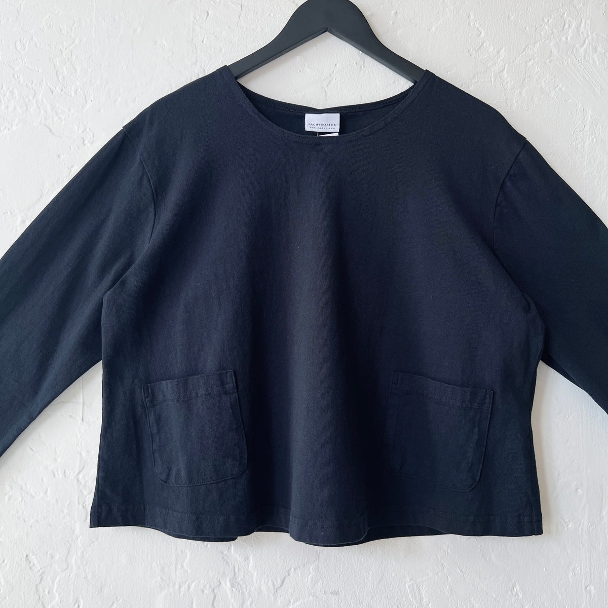 Black long-sleeve shirt on a hanger against a white wall