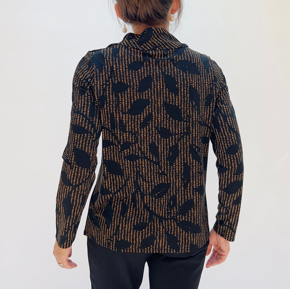 Person wearing a patterned shirt with long sleeves on a white background, shot from behind.