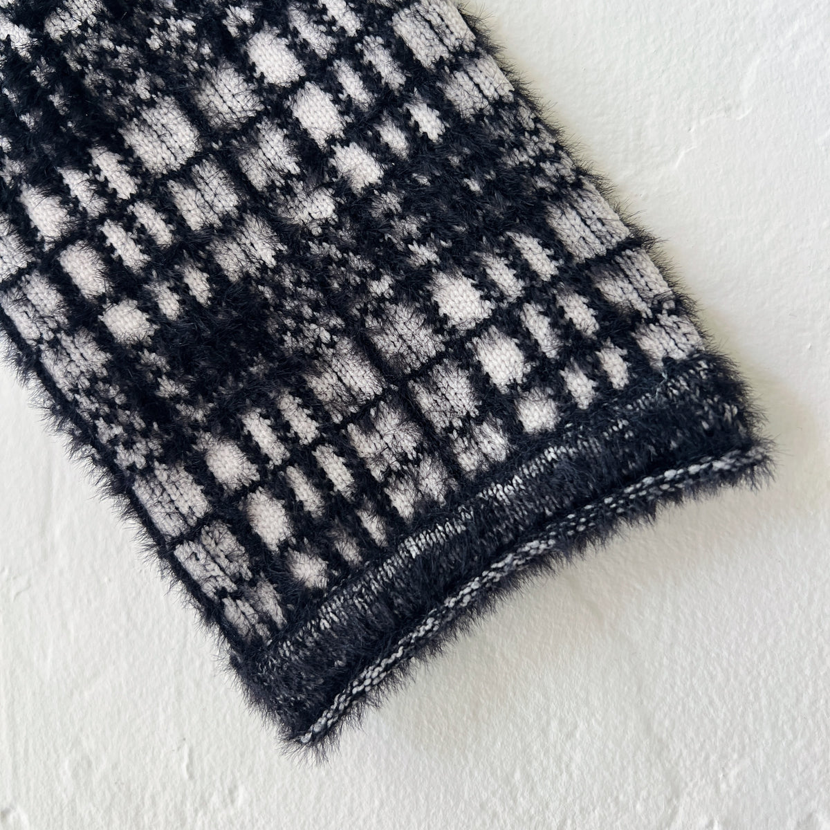 Close-up detail of Habitat Plaid Patchwork Cardigan sleeve and ribbed cuff showing windowpane plaid knit in black and cream with soft eyelash-textured nylon blend fabric and knitted hem trim
