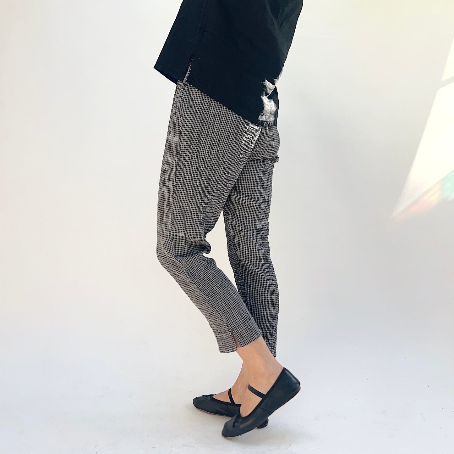 Person wearing gray and black checkered pants and black shoes on a white background, viewed from the side