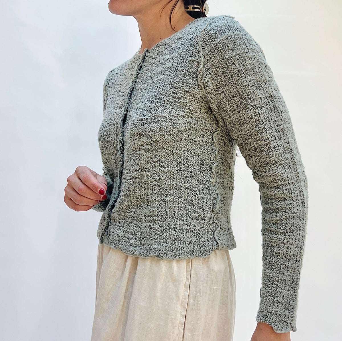 Person wearing a textured gray cardigan against a white background, viewed from the side