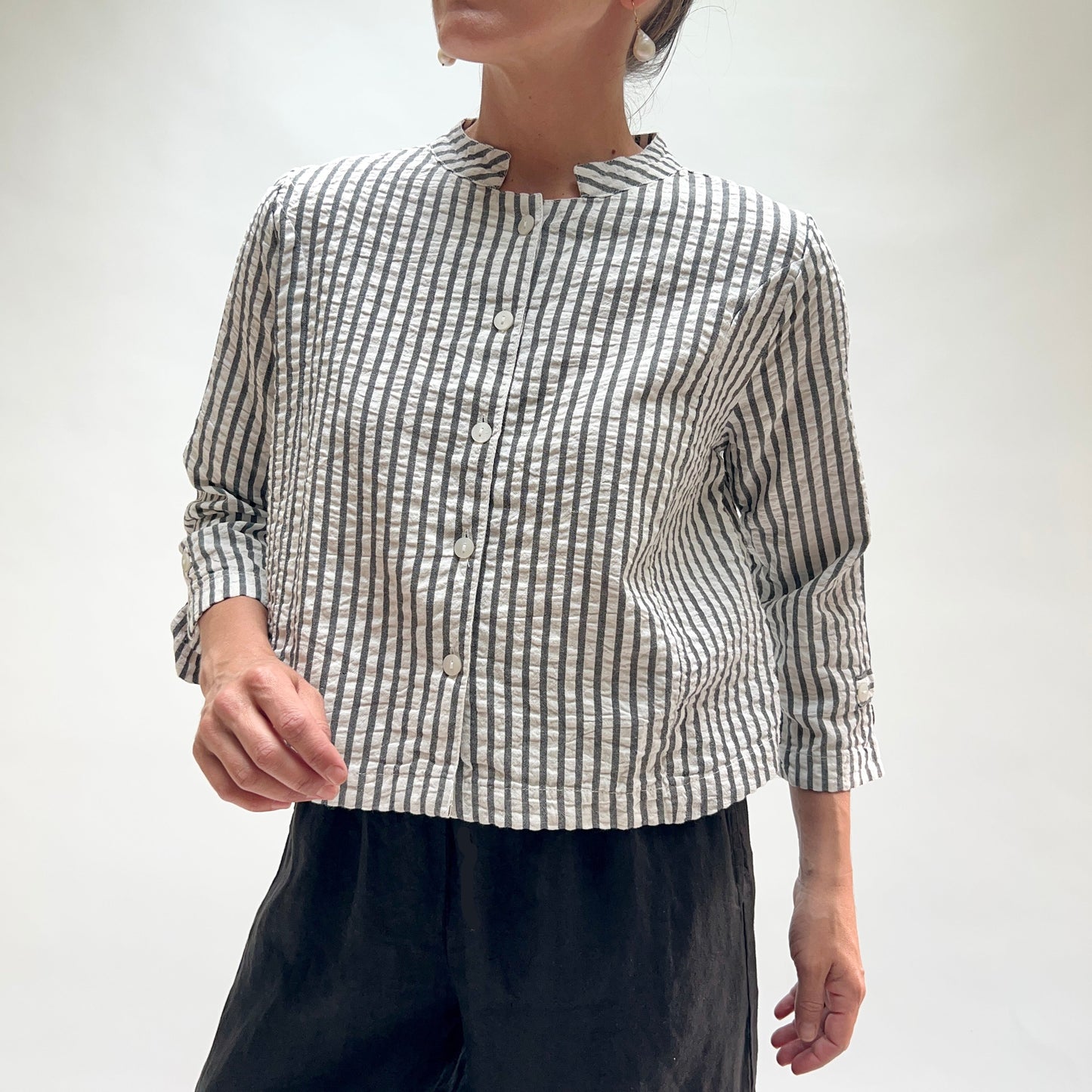 Person wearing a black and white striped shirt with rolled-up sleeves on a plain background