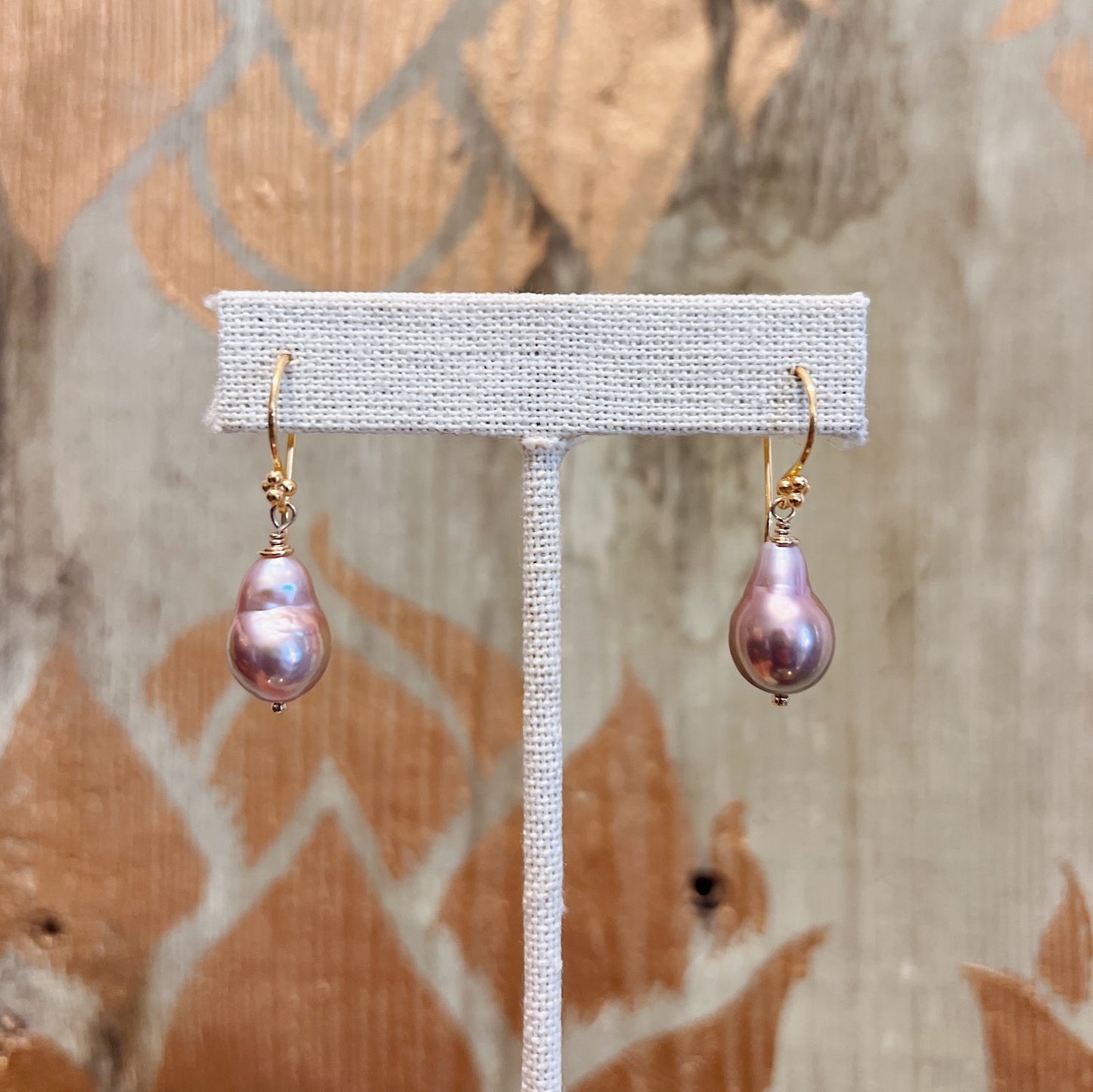 Champagne baroque pearl drop earrings on gold vermeil French hook findings, displayed on a linen earring stand against a rustic wood background