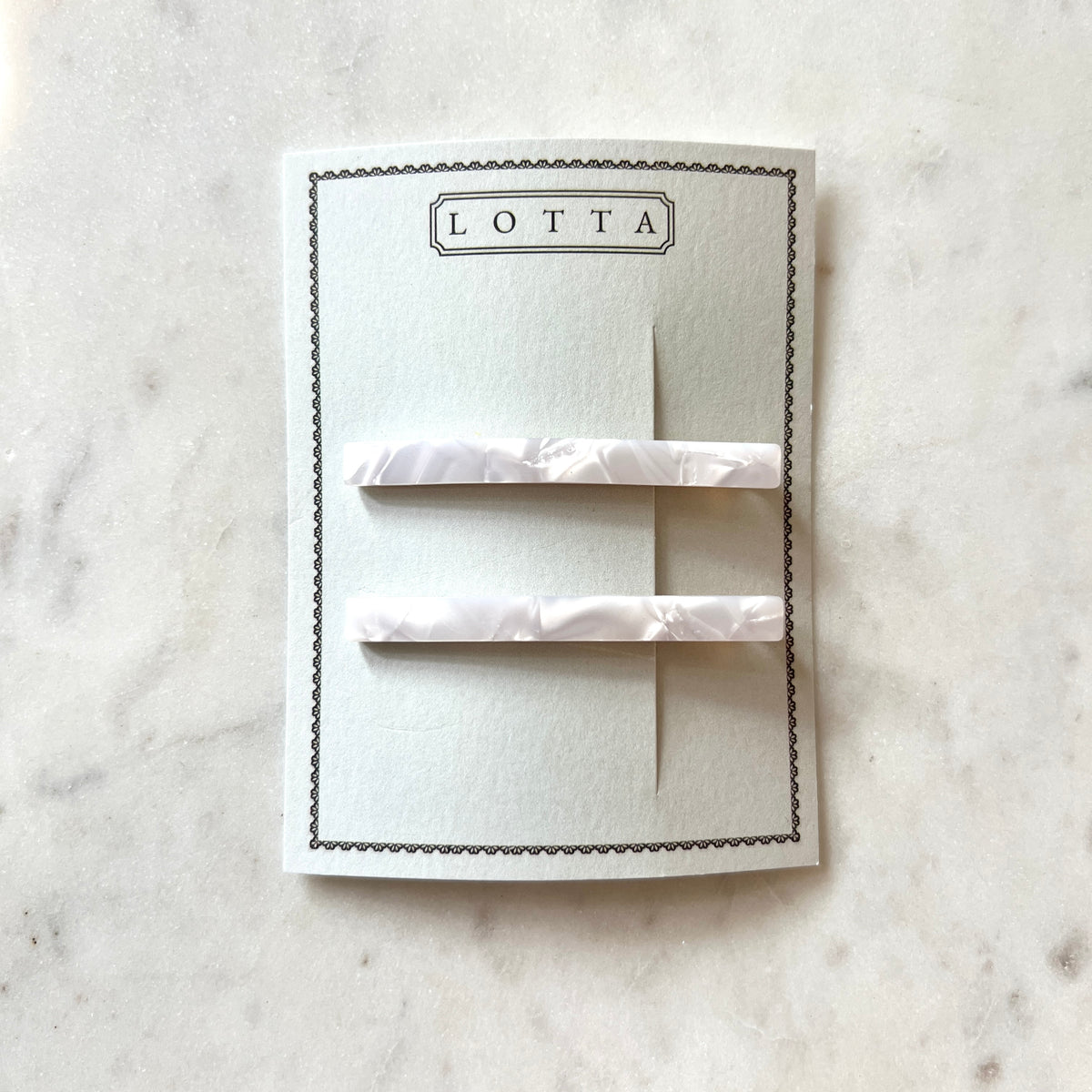 Two white hair clips on a Lotta branded card against a marble background