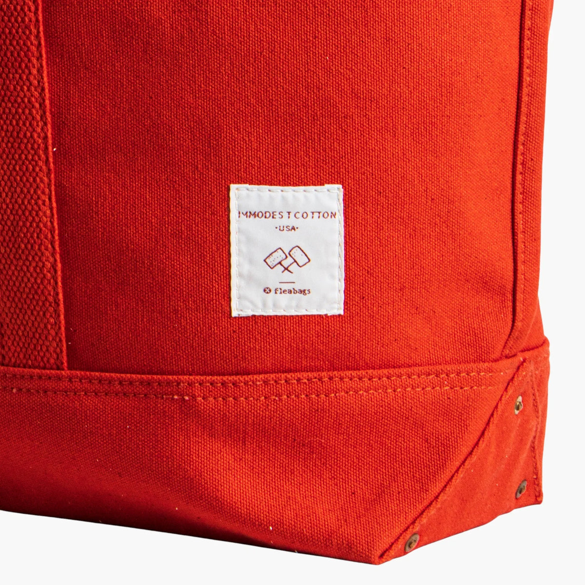 Close-up of the white Immodest Cotton label, double stitching, and riveted bottom corner on the Persimmon tote.