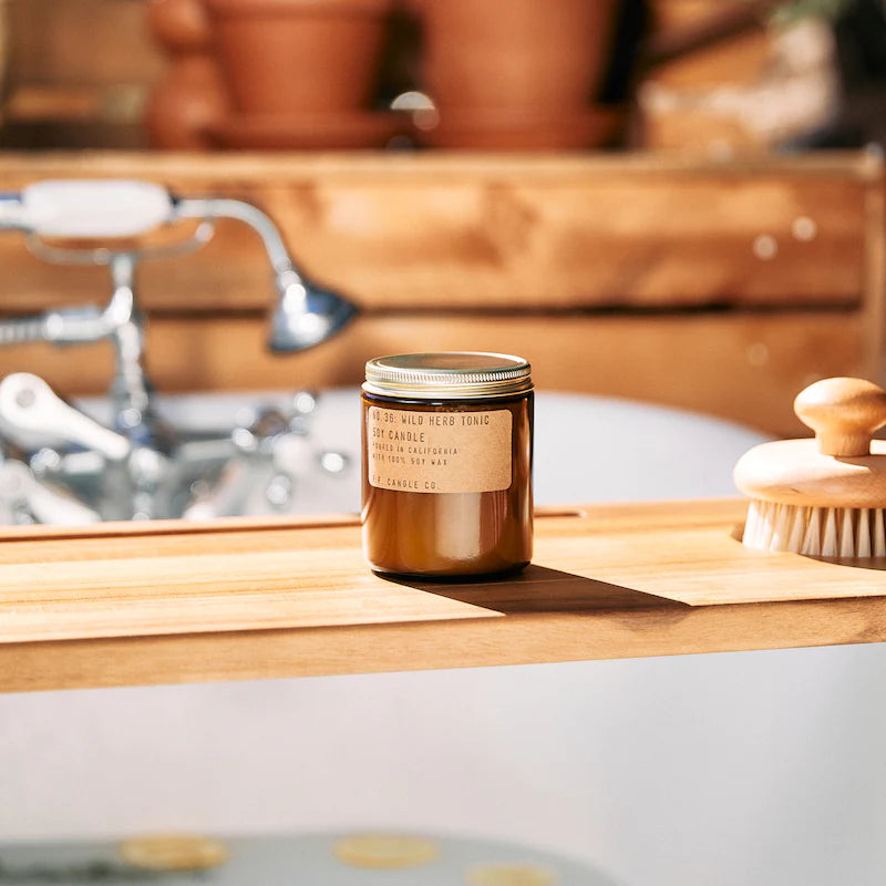 Wild Herb Tonic candle on a sunlit wooden counter beside a sink and scrub brush.