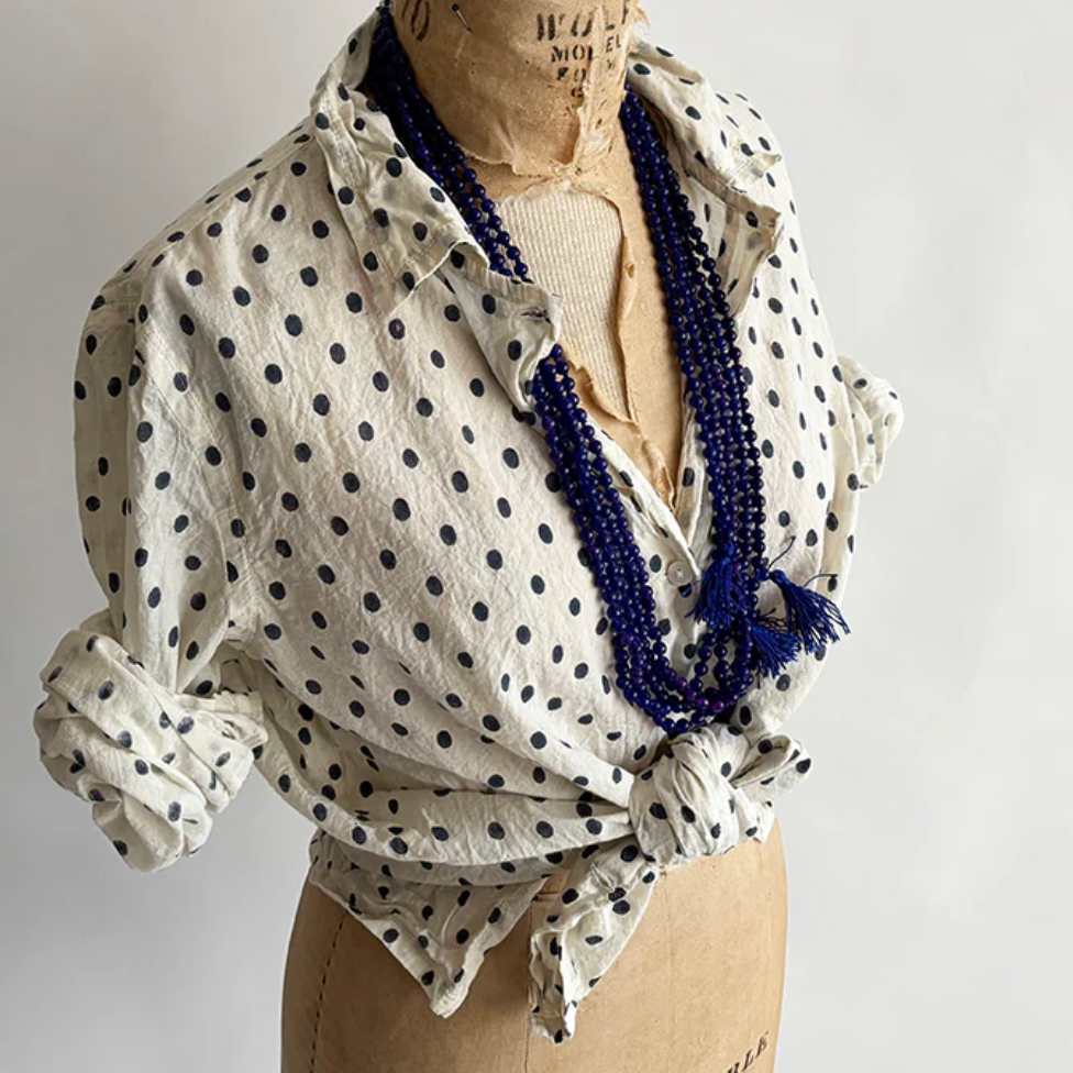 White polka dot shirt with blue beads on a mannequin against a gray background