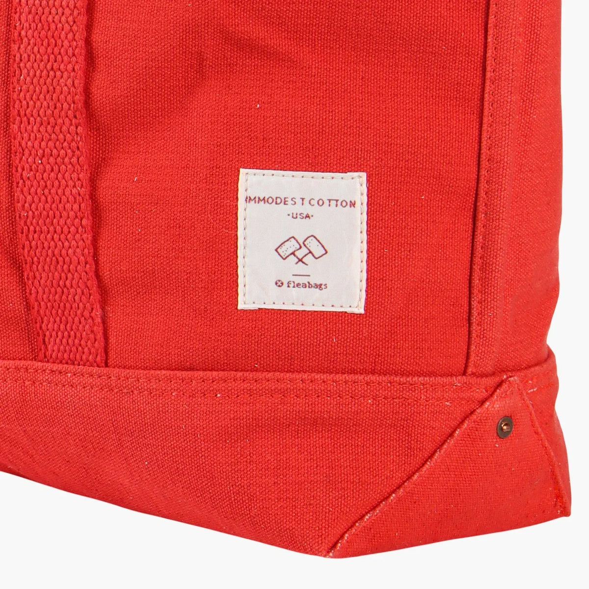 Close-up of the white Immodest Cotton label, stitching, and riveted bottom corner on the Persimmon tote.