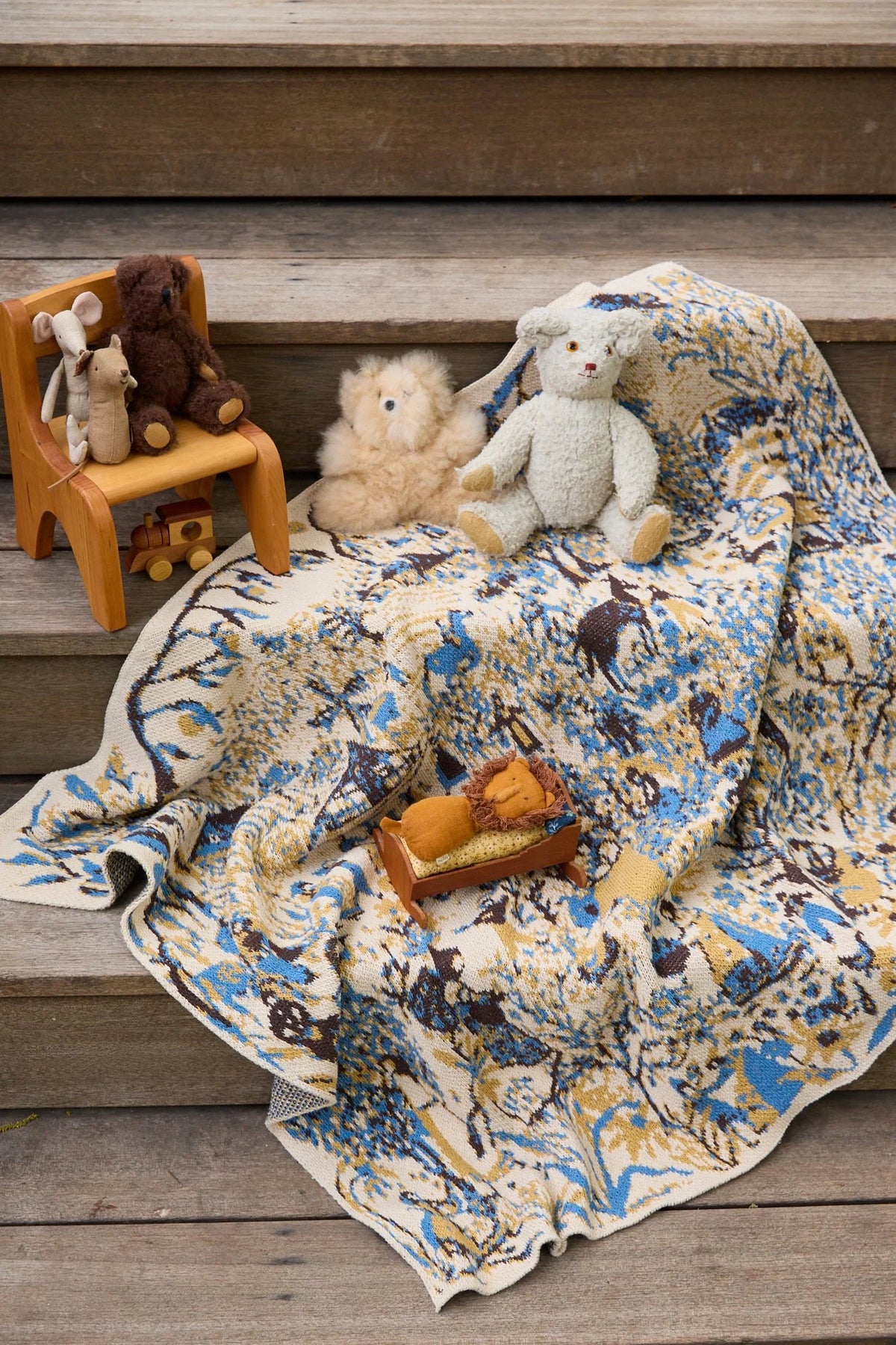 Farmscape Straw child blanket draped over wooden steps with stuffed animals and miniature wooden furniture.