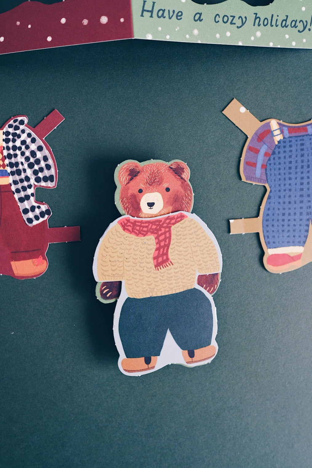 Small Adventure Bear Paper Doll Cozy Holiday Card, close-up of the paper bear wearing a yellow sweater, red scarf, and blue pants.