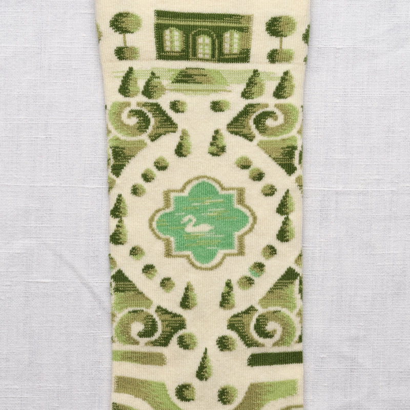A close-up of the ankle of the socks with green and beige patterned fabric with a central design on a light gray background