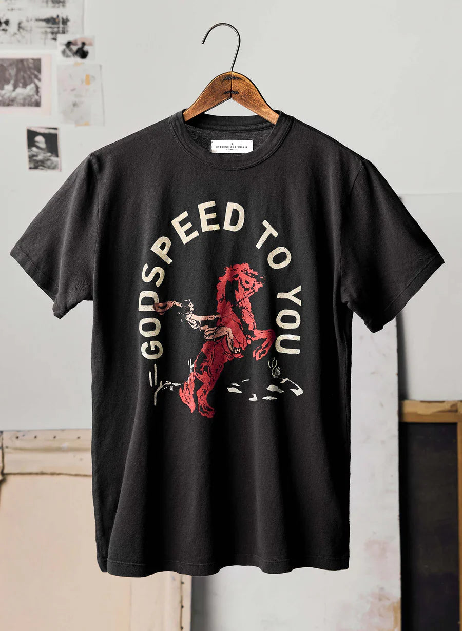 The Godspeed Tee by Imogene + Willie on a wooden hanger in a studio setting, showing the full front with a screen-printed graphic of a rearing red horse with rider and the text 'GODSPEED TO YOU' in cream arched lettering on a black cotton tee