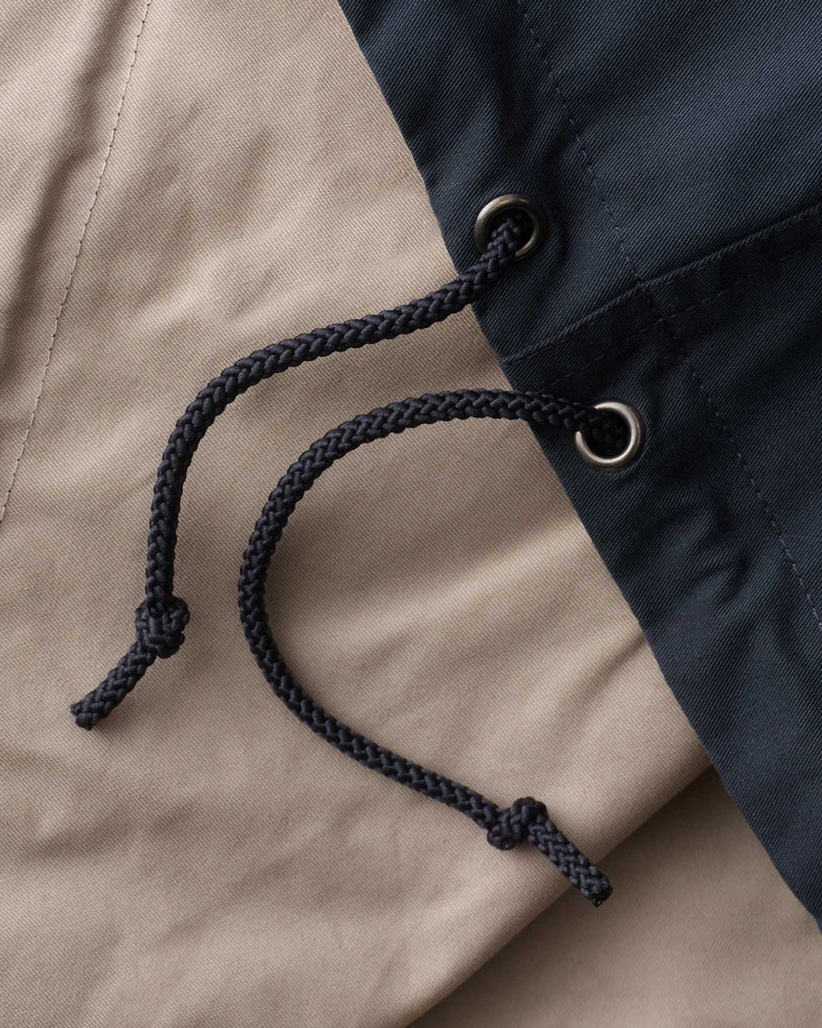 Extreme close-up of braided navy drawcord through metal grommets showing both fabric sides