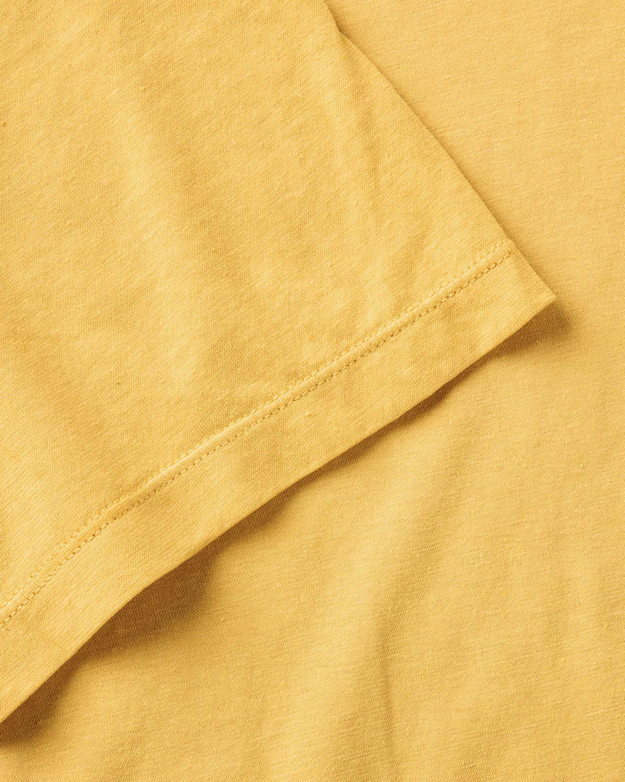 Close-up detail of Taylor Stitch Cotton Hemp Tee sleeve hem showing stitching and soft organic cotton fabric texture in Goldfinch yellow