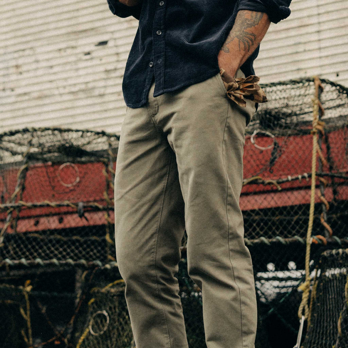 Person wearing a dark shirt and beige pants standing in front of stacked lobster traps.