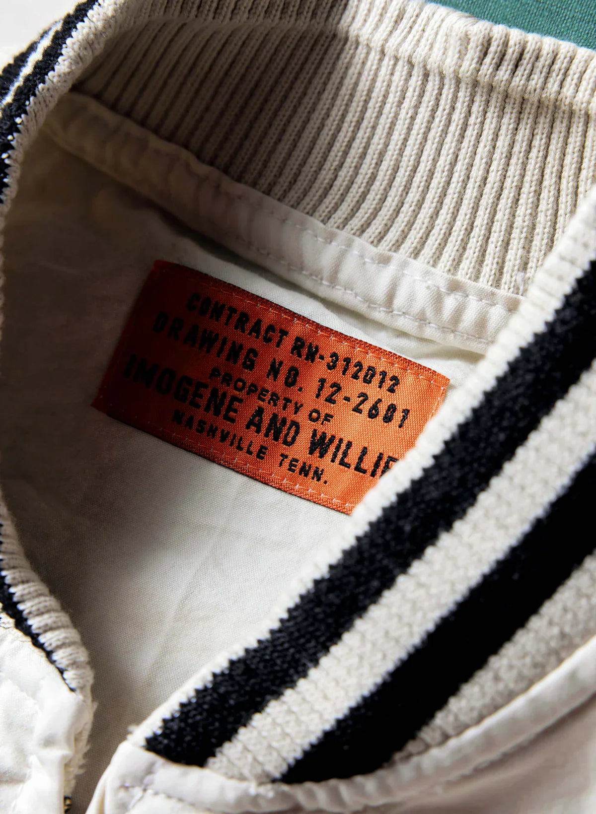 Close-up of the interior collar of The Madisonville Jacket showing the orange Imogene and Willie contract label reading 'Property of Imogene and Willie, Nashville Tenn.' and the black and white striped rib neckband