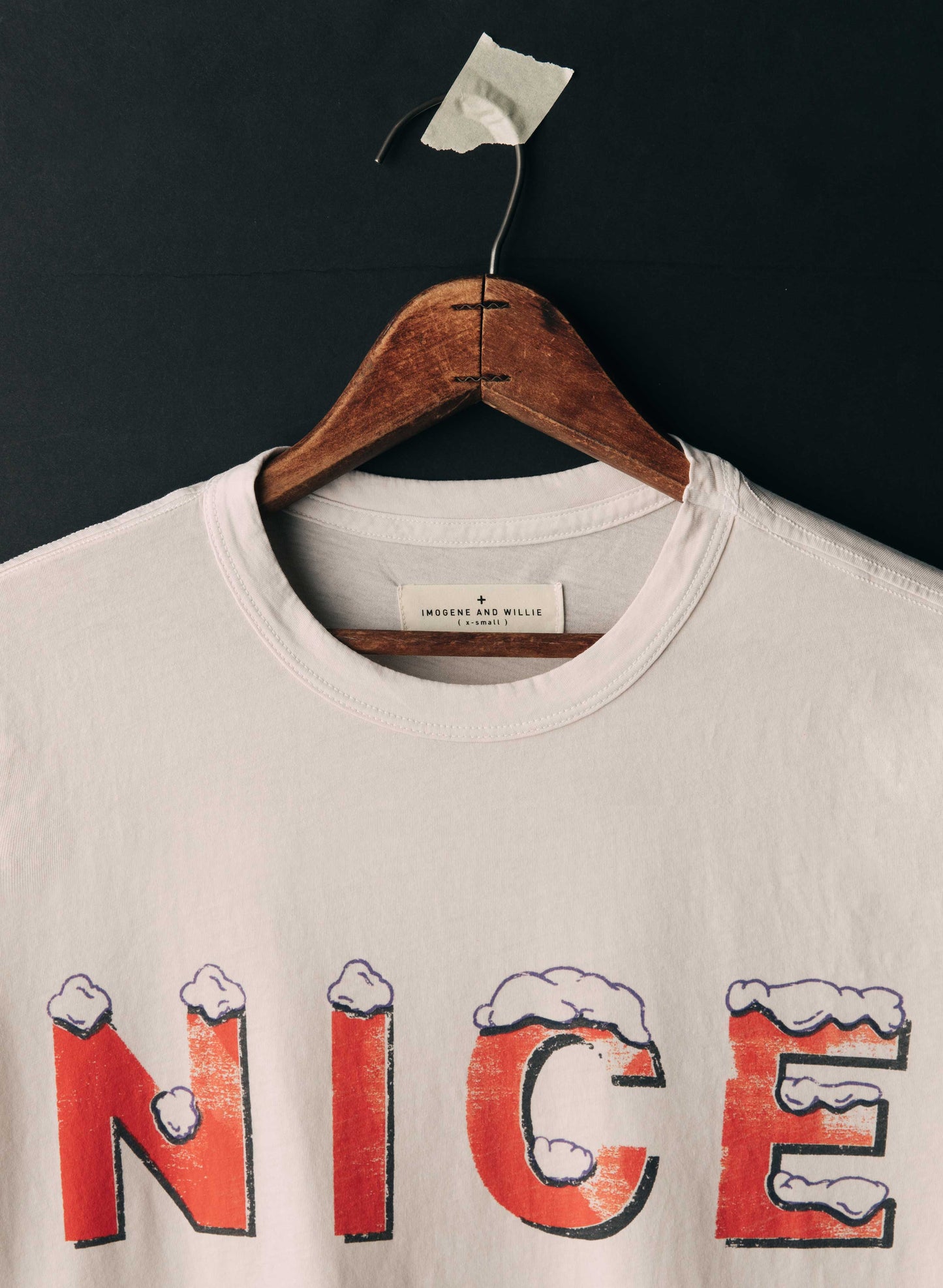 Close-up of the neckline of The Nice Tee by Imogene + Willie showing the woven label, ribbed crew neck, and the top of the screen-printed 'NICE' graphic in red vintage lettering with snow detail on white cotton