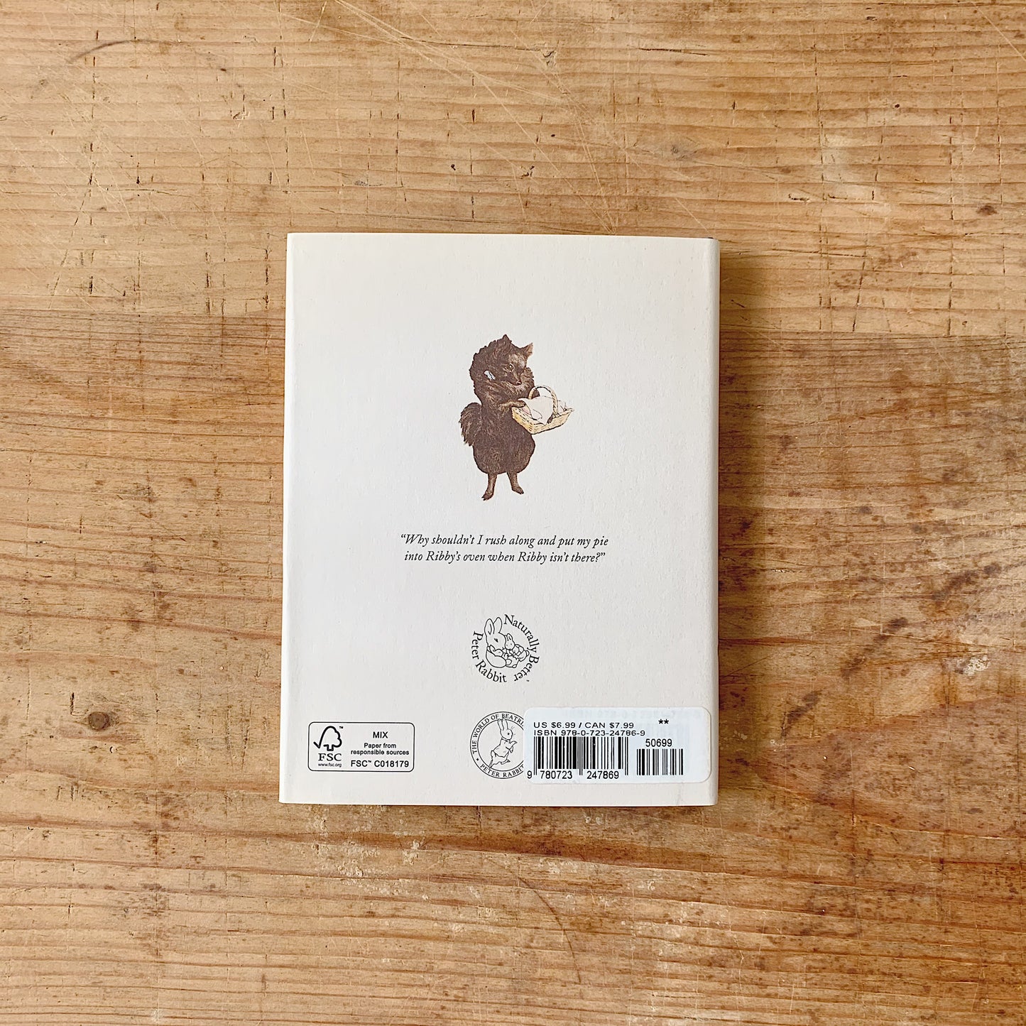 The back cover of the book with an illustration of an animal holding a basket, shown on a wooden surface