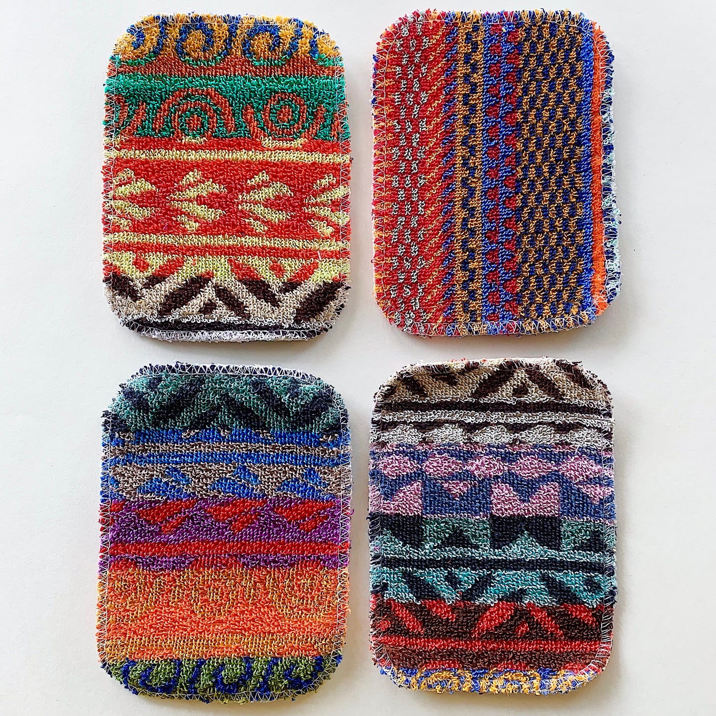 Four scrubby pad sponges lying side by side as seen from above. They are colorful and made up of unique patterns.