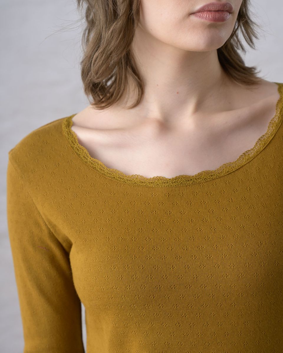 Close detail of the neckline of the BIBICO Cali Pointelle Tee in Bronze, showing the scalloped lace trim on the scooped neckline and the all-over pointelle eyelet texture of the organic cotton jersey in rich bronze-mustard gold
