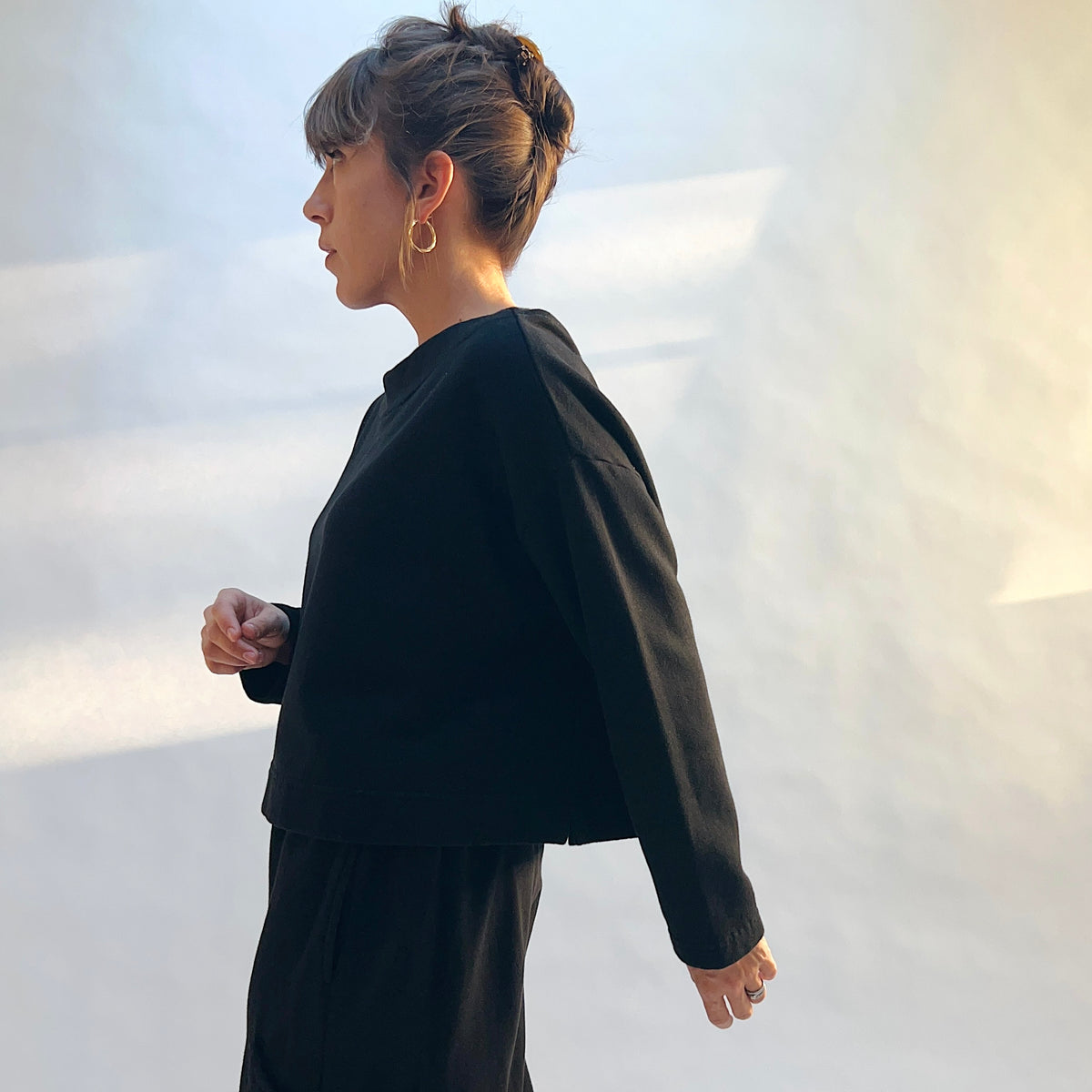 Side view of Button Back Fleece Pullover in Black, showing the loose silhouette, cropped length, and long sleeves.
