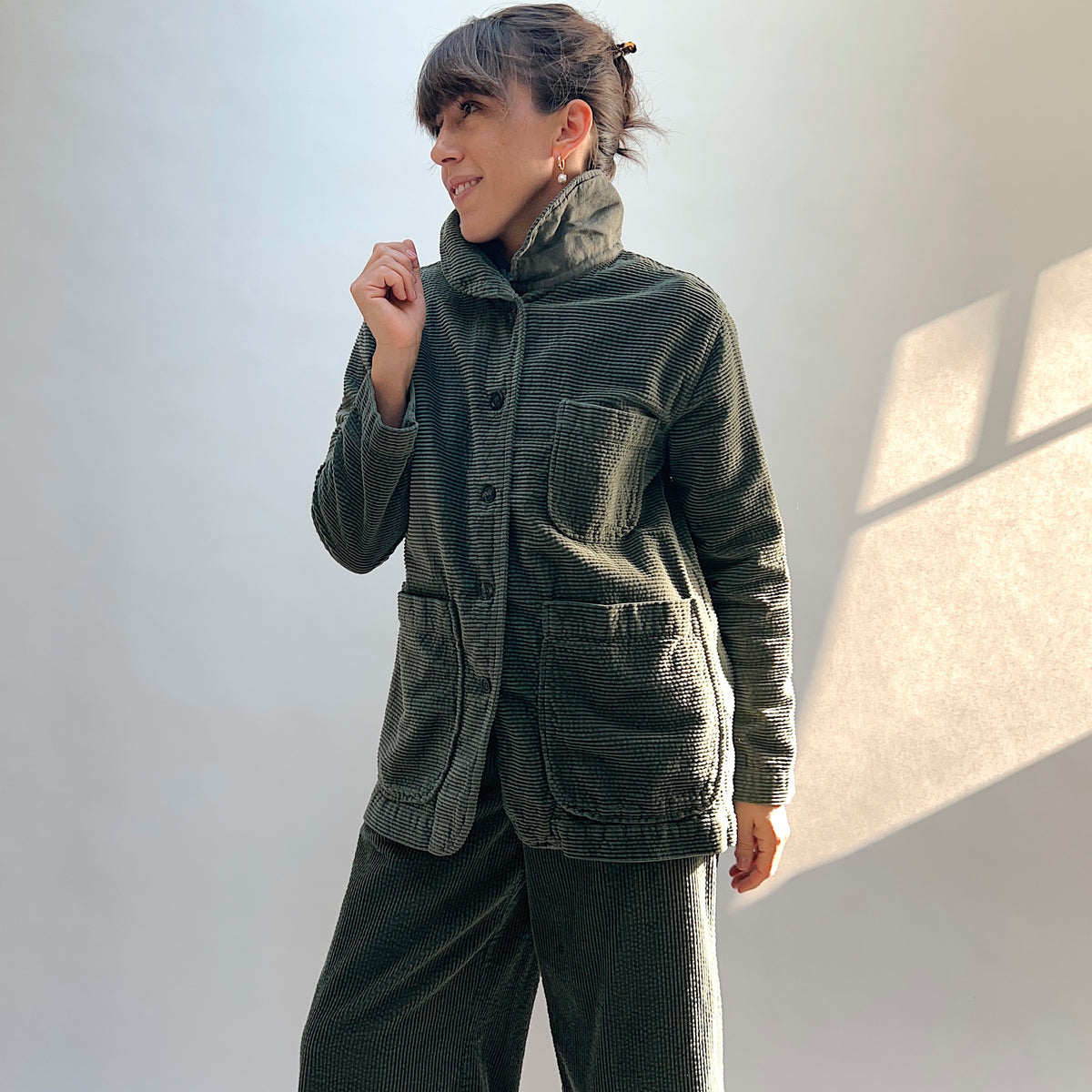 Model wearing the Cut Loose Lux Corduroy Long Blazer in Kelp with the collar raised, showing the button front and patch pockets.
