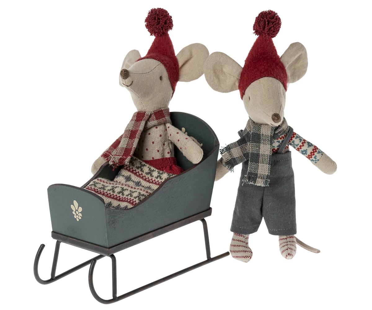 Miniature green sleigh with one toy mouse seated inside and another standing beside it, both wearing red hats and scarves. Mice not included.
