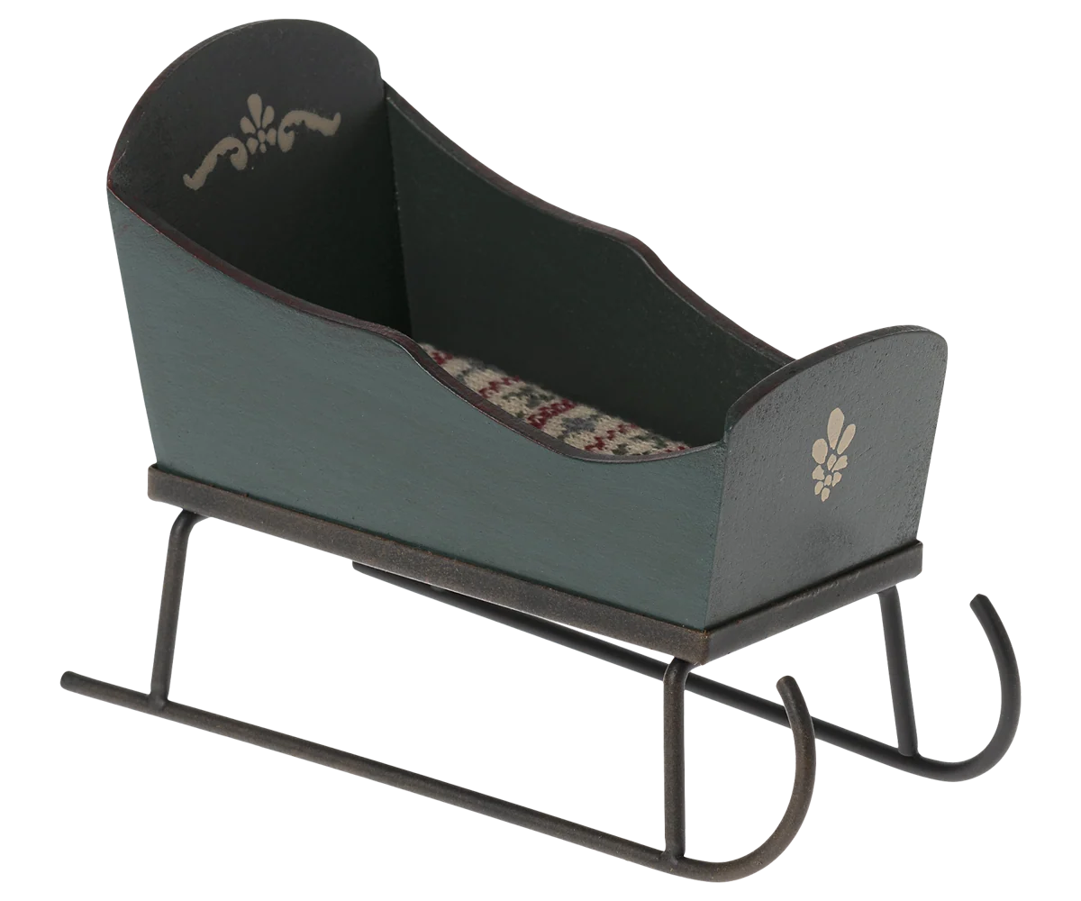 Maileg miniature green sleigh with cream painted motifs, curved metal runners, and a patterned mattress.

