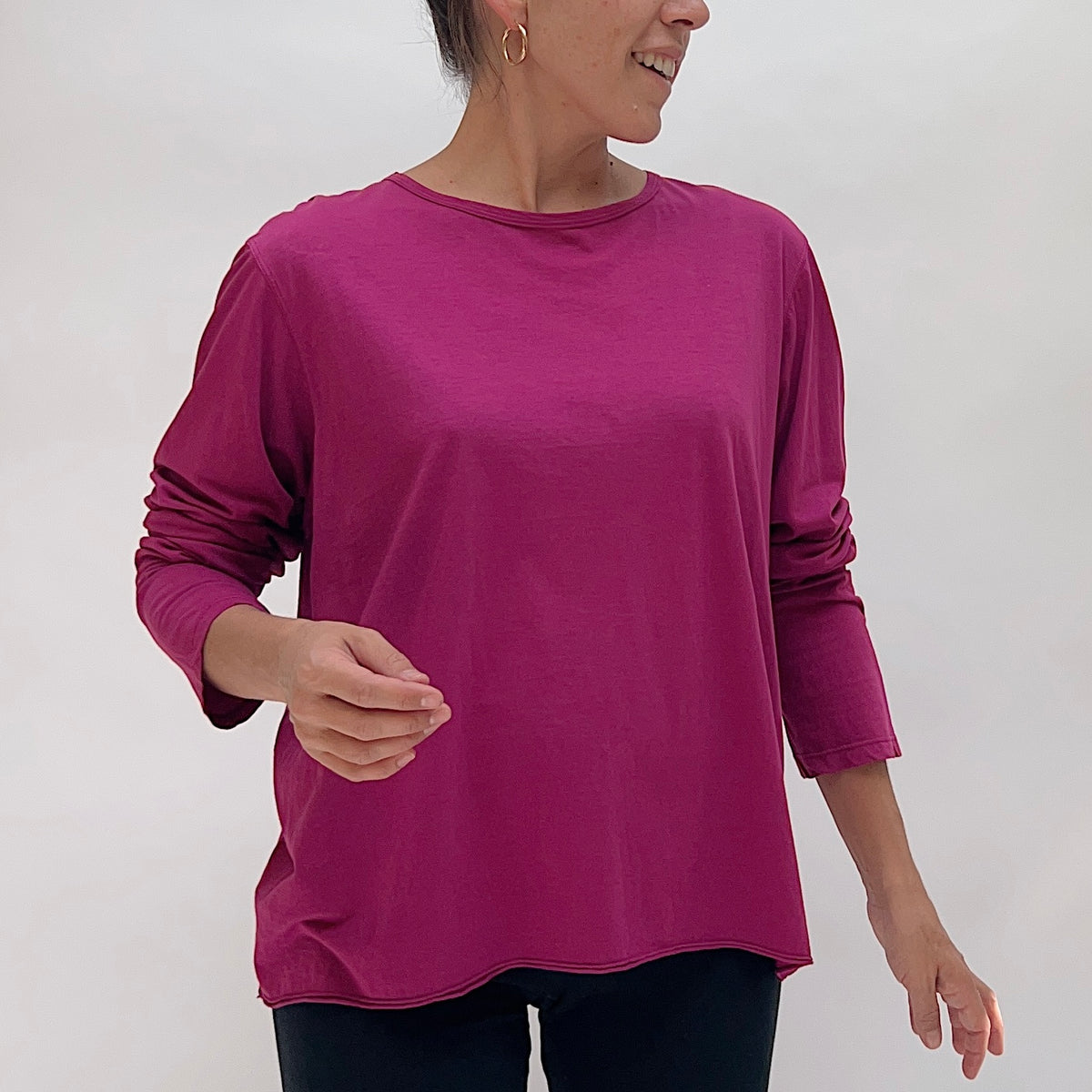 Model wearing the North Star Base Tissue Cotton Long Sleeve Agnes Tee in Raspberry from the front, showing the relaxed boxy silhouette, crew neckline, and curved lettuce-edge hem in rich magenta raspberry tissue cotton, paired with dark trousers
