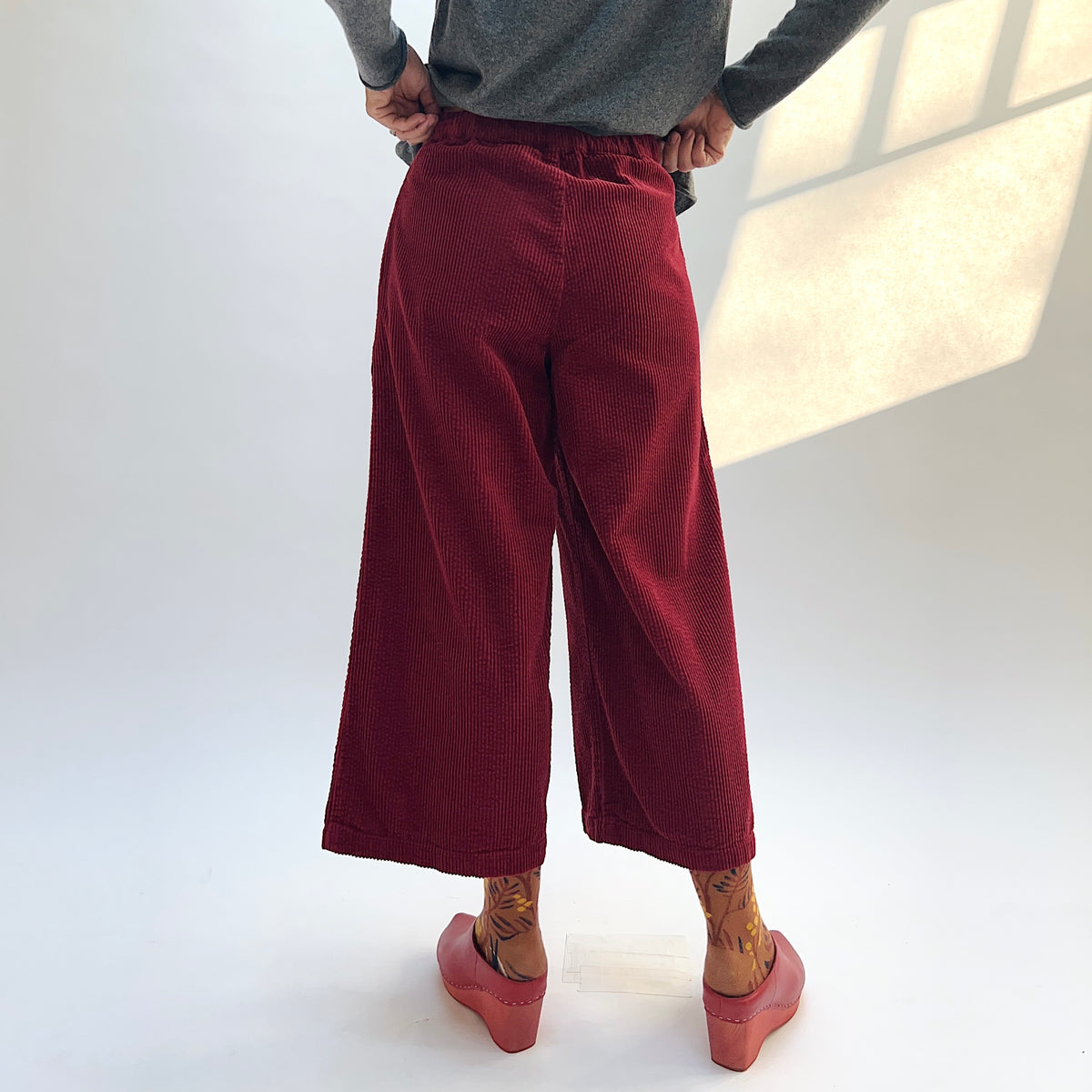 Back view of the Lux Corduroy Crop Wide Leg Pant in Maraschino on a model, showing the waistband and cropped wide legs.
