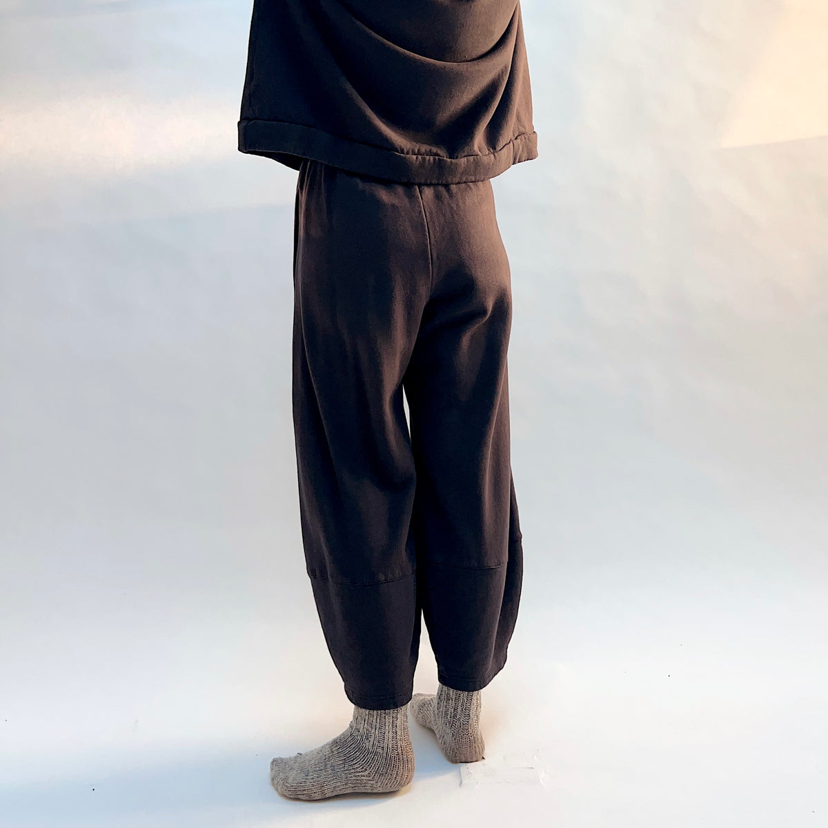Angled back view of Oliver Fleece Pant in Fig, showing the loose silhouette and horizontal lower-leg seams.
