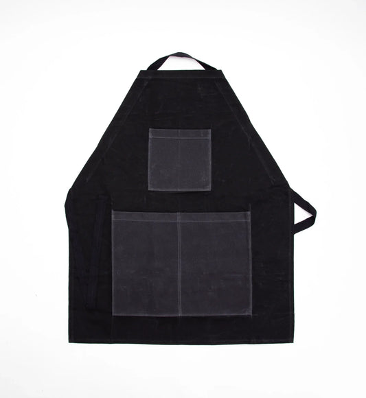 Black waxed cotton apron with contrasting gray chest and divided lower pockets, a black neck strap, and waist ties.
