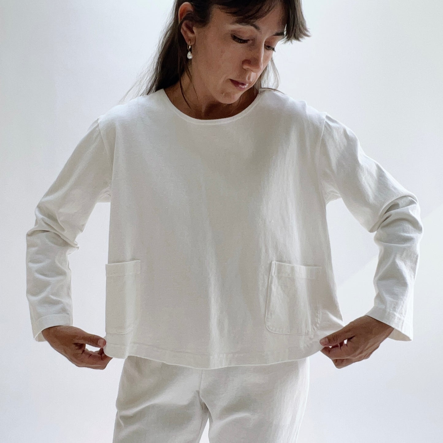 Back view of model wearing a cream boxy cotton top with a relaxed silhouette and clean seam detail, paired with cream trousers.
