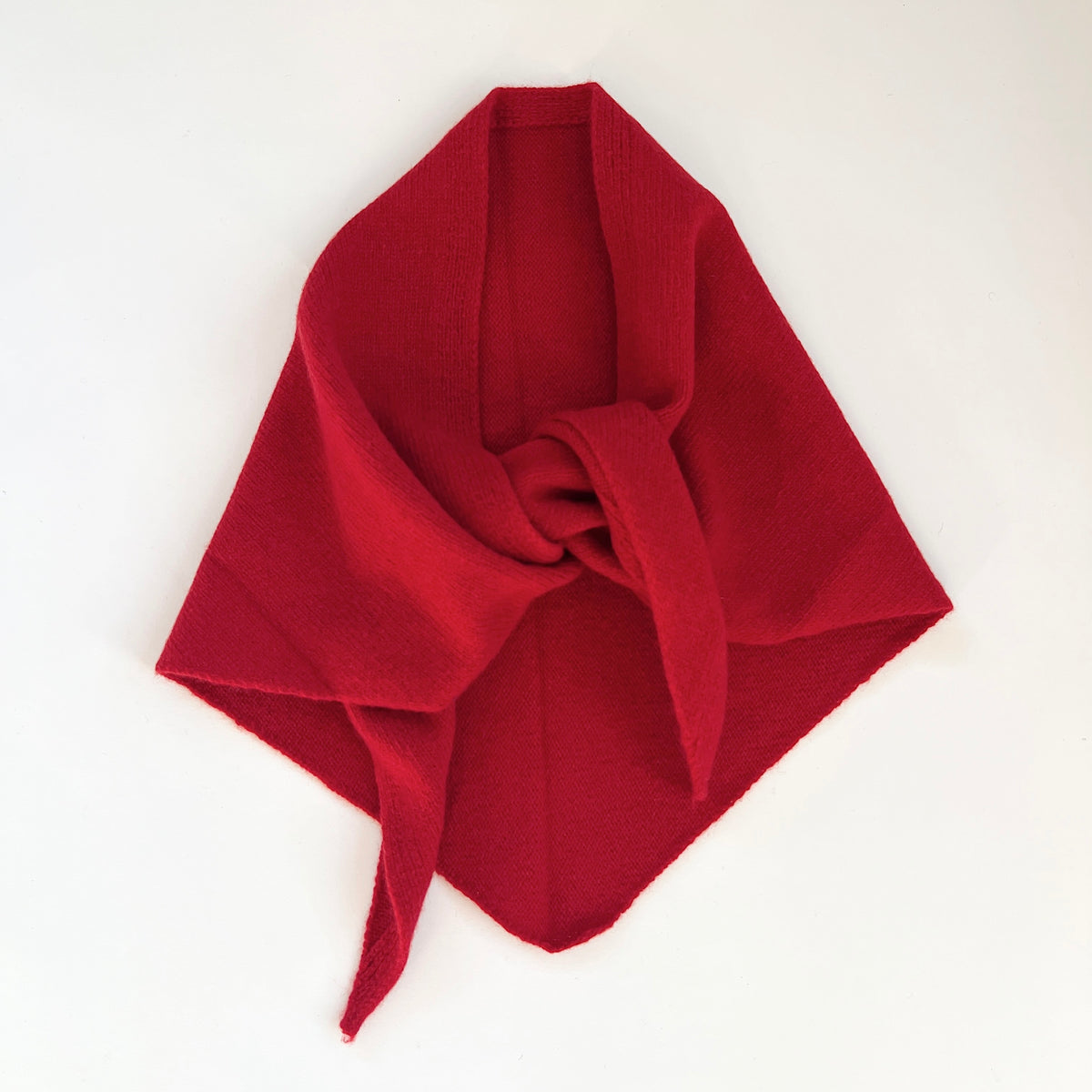 Flat lay view of the red merino wool triangle scarf arranged with a loose knot and pointed ends.
